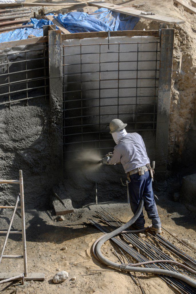 A person using a high-pressure shotcrete nozzle and hose.