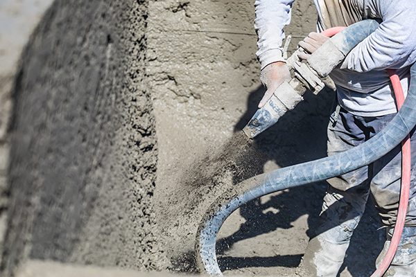 A worker shoots shotcrete through a hose to form a pool.